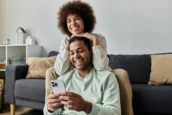Young African American woman sitting near her husband with hearing aid and looking at phone. — Stock Photo