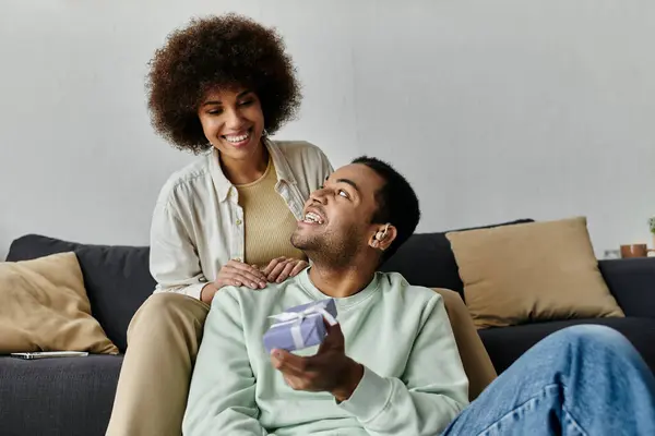 Attractive African American woman near her husband with hearing aid, gift in hands. — Stock Photo