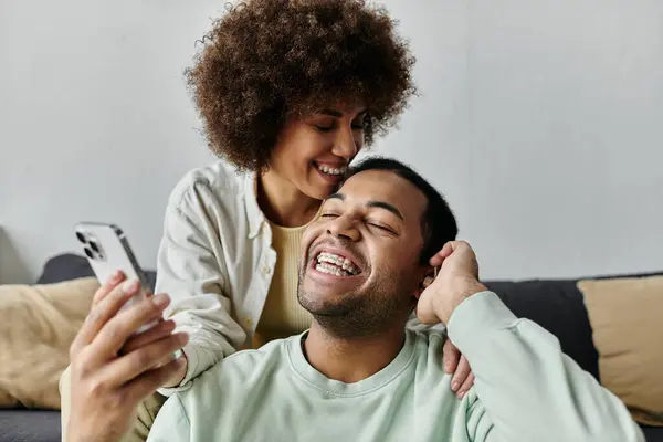 Femme afro-américaine élégante assise près de son mari avec aide auditive et regardant le téléphone. — Photo de stock