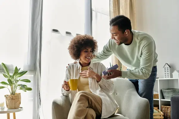 Appealing African American woman near her husband with hearing aid, gift in hands. — Stock Photo