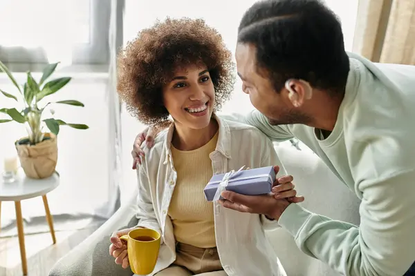 Hübsche Afroamerikanerin neben ihrem Mann mit Hörgerät, Geschenk in der Hand. — Stockfoto