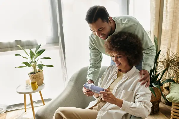 Mujer afroamericana alegre cerca de su marido con audífono, regalo en las manos. - foto de stock