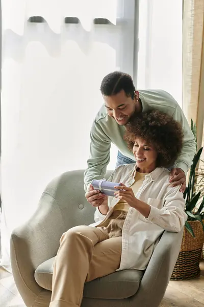 Feliz mujer afroamericana cerca de su marido con audífono, regalo en las manos. - foto de stock