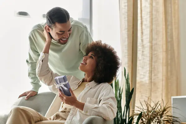 Fürsorgliche Afroamerikanerin in der Nähe ihres Mannes mit Hörgerät, Geschenk in der Hand. — Stockfoto