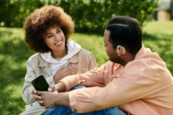 Um feliz casal afro-americano se comunica em linguagem gestual enquanto está sentado em um gramado gramado. — Fotografia de Stock