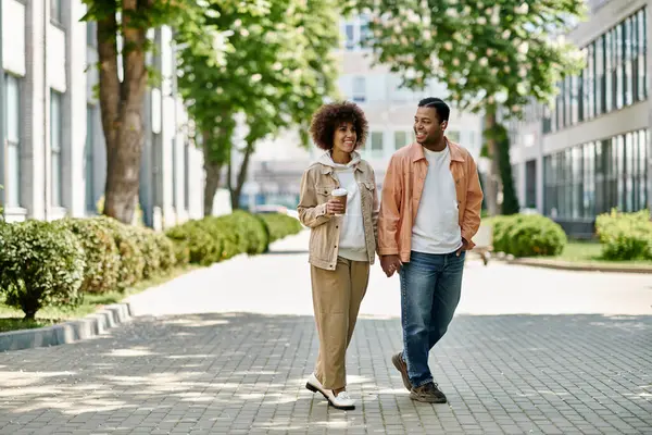 A young African American couple walks hand-in-hand along a paved walkway, enjoying a bright, sunny day. — Stock Photo