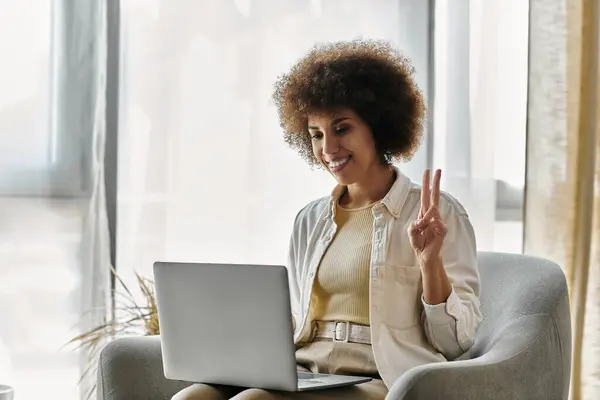 A woman sits in a chair, smiling as she uses sign language while looking at a laptop. — Stock Photo
