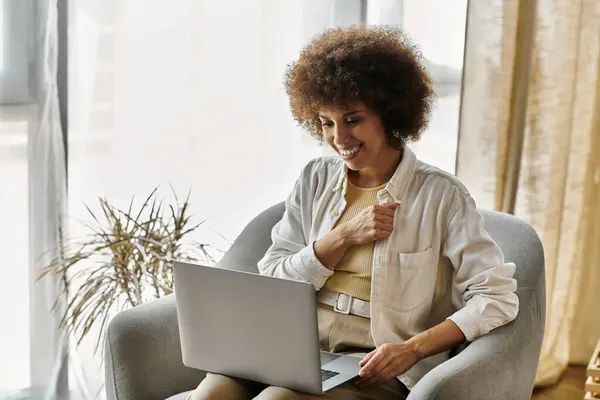 A woman sits in an armchair, smiling warmly while using sign language, next to laptop. — Stock Photo