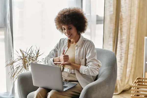 An African American woman signs with her hands while sitting in a chair and using a laptop. — Stock Photo