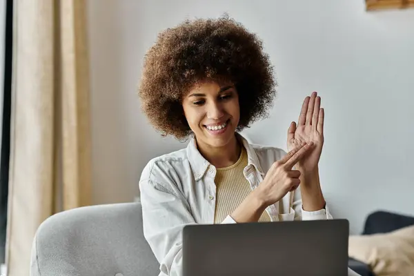 A young African American woman uses sign language to communicate while sitting on a couch at home, next to laptop. — Foto stock