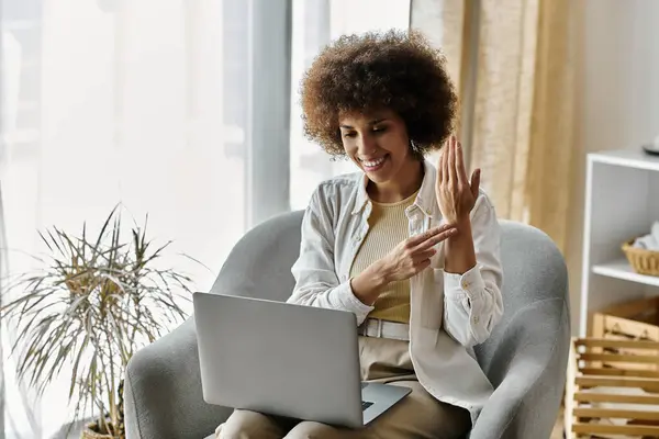 An African American woman communicates with sign language while sitting on a couch at home, next to laptop. — Stock Photo