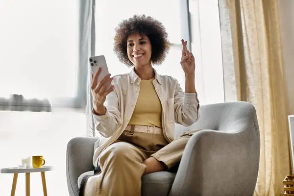 A woman sits in a chair at home, smiling and holding a smartphone. — Stock Photo