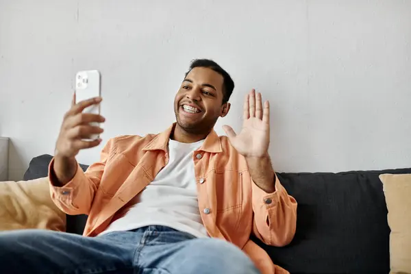 Um homem senta-se em um sofá, sorrindo enquanto usa a linguagem gestual para ter uma conversa em seu telefone. — Fotografia de Stock