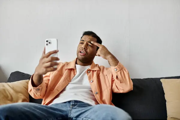 Um homem senta-se em um sofá, usando linguagem gestual enquanto conversa por vídeo em seu telefone. — Fotografia de Stock