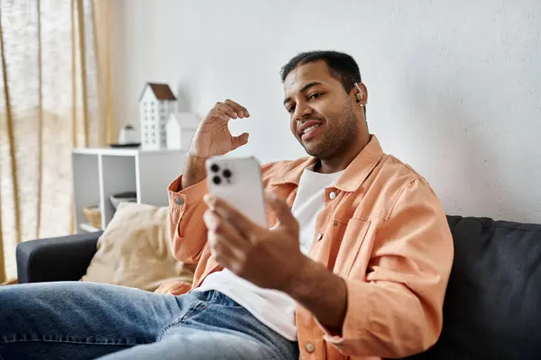 A man sits on a couch and uses sign language while holding a smartphone. — Stock Photo