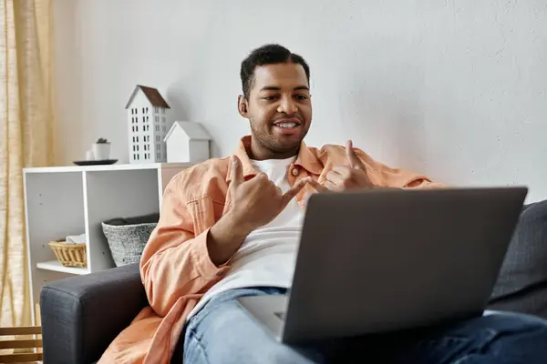 Um homem senta-se em um sofá em sua sala de estar, usando linguagem gestual para se comunicar enquanto usa um laptop. — Fotografia de Stock