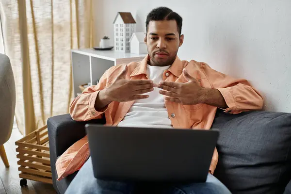 A man sits on a couch, using sign language while looking at a laptop. — Stock Photo