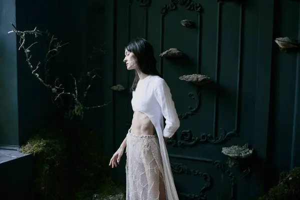 A woman in a white dress poses in front of a dark green background with decorative elements. — Stock Photo