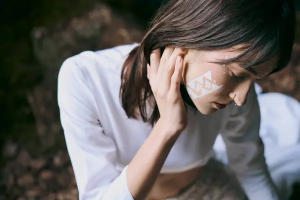 A woman with white paint on her face sits near a swamp. — Stock Photo