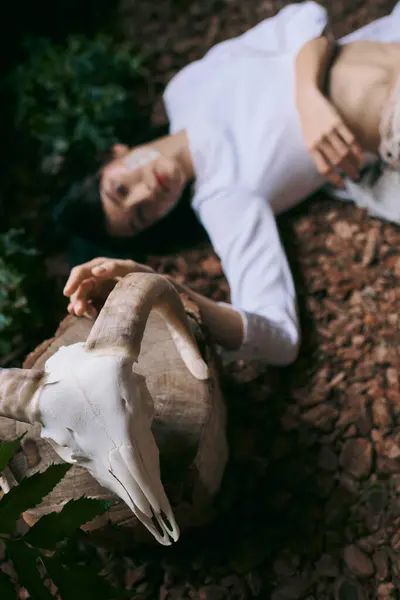 Eine Frau liegt in einem sumpfigen Wald, ihre Hand ruht auf einem weißen Schädel. — Stockfoto