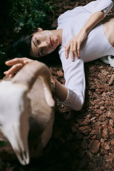 A woman in white clothing lies on a bed of fallen leaves, her gaze directed towards the camera. — Stock Photo