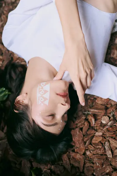 A young woman rests peacefully in a forest setting surrounded by fallen leaves and branches. — Stock Photo