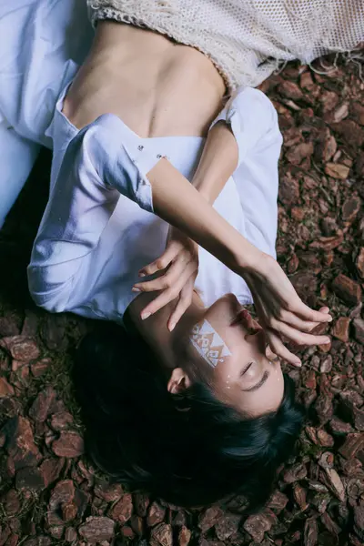 A woman in white lies near swamp, her face obscured by a geometric design. — Stock Photo