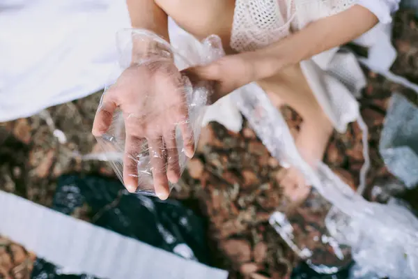 A womans hand holds a piece of plastic near a swamp filled with garbage. — Stock Photo