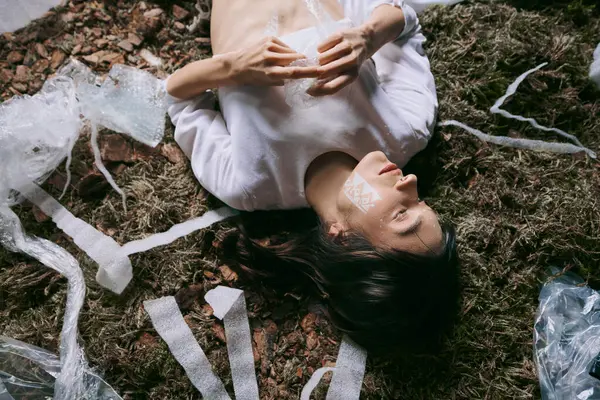 A woman lies amongst a field of plastic waste, a stark contrast to her aesthetic attire. — Stock Photo