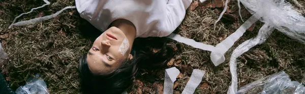 A woman in white clothing lies amidst a swamp overflowing with plastic waste. — Stock Photo