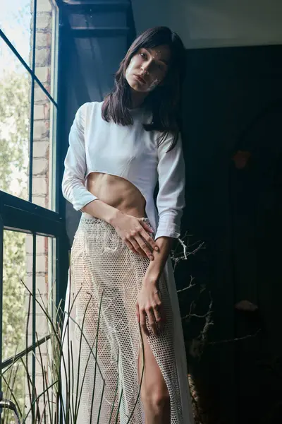 A woman in a white dress poses by a window overlooking a swamp. — Stock Photo