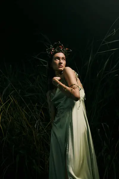 A woman in a flowing green dress poses near a swamp at night. — Stock Photo
