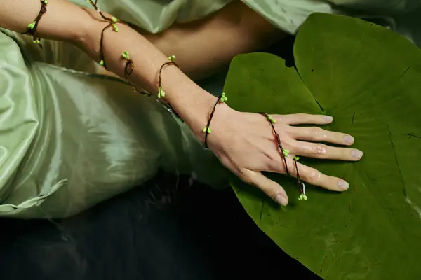 A womans hand adorned with a delicate green bracelet rests on a large lily pad. — Stock Photo
