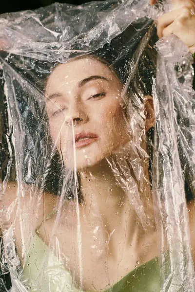 A woman poses with plastic draped over her, her eyes closed and her expression serene. — Stock Photo