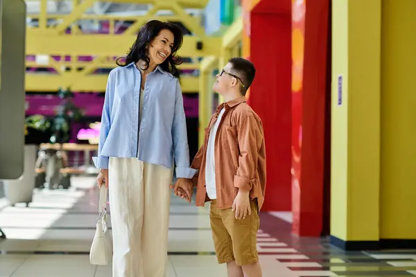 A mother and her son with Down syndrome walk hand-in-hand through a shopping mall, enjoying a day out together. — Stock Photo