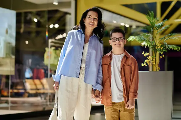 A mother and her son with Down syndrome enjoy a day out together, walking through a brightly lit shopping mall. — Stock Photo