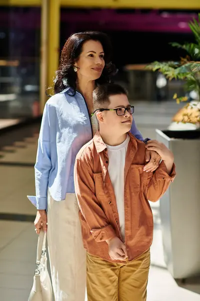 Una madre y su hijo con síndrome de Down caminan codo con codo por un centro comercial, disfrutando de un día juntos.. - foto de stock
