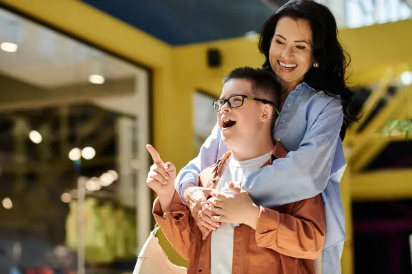 A mother and her son with Down syndrome share a laugh while walking through a shopping mall. — Stock Photo