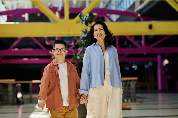 Una madre e suo figlio con la sindrome di Down sorridono mentre camminano mano nella mano attraverso un centro commerciale.. — Foto stock