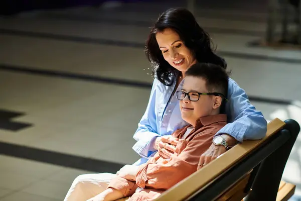 A mother and her son with Down syndrome share a moment of tenderness while sitting on a bench in a shopping mall. — Stock Photo