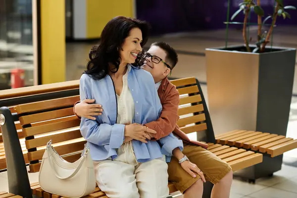 A mother and her son with Down syndrome are enjoying a day out at the mall, sharing a moment of laughter and warmth on a bench. — Stock Photo