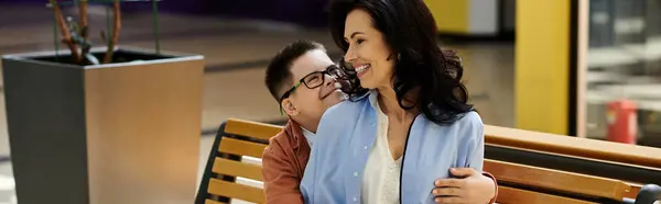 A mother and her son with Down syndrome share a joyful moment together while sitting on a bench in a shopping mall. — Stock Photo