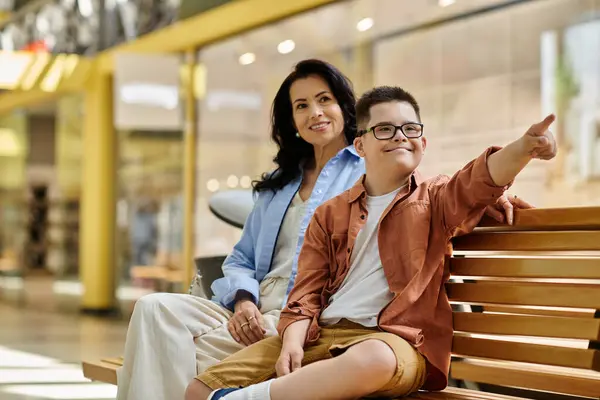 A mother and her son with Down syndrome share a moment of joy and laughter while sitting on a bench in a shopping mall. — Stock Photo