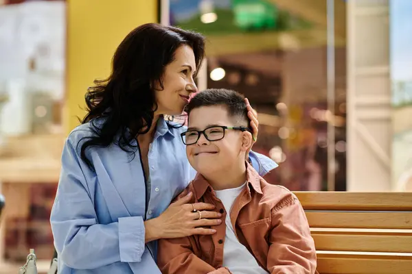 A mother and her son with Down syndrome share a tender moment while sitting on a bench in a shopping mall. — Stock Photo