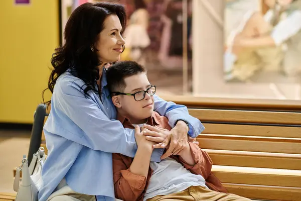 A mother and her son with Down syndrome share a tender moment while sitting on a bench in a shopping mall. — Stock Photo