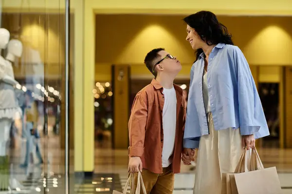 A mother and her son with Down syndrome walk through a shopping mall, enjoying a day out together. — Stock Photo