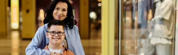 A mother and her son with Down syndrome smile for the camera while walking through a shopping mall. — Stock Photo