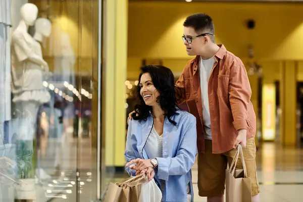 Uma mãe e seu filho com síndrome de Down caminham através de um shopping, olhando para as exposições. — Fotografia de Stock