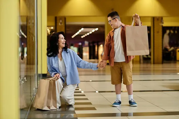 A mother and her son with Down syndrome enjoy a shopping trip at the mall, walking hand-in-hand and carrying bags. — Stock Photo