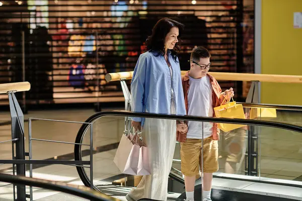 Una madre e suo figlio con la sindrome di Down camminano mano nella mano su una scala mobile in un centro commerciale.. — Foto stock